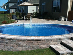 Round semi in-ground pool with custom stonework exterior walls and matching steps/patio.